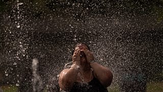 Una donna si rinfresca in una fontana in un parco lungo il fiume a Madrid, in Spagna, mercoledì 15 giugno 2022.