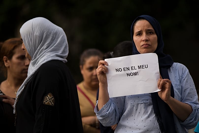 Una mujer sostiene una pancarta que reza en catalán: "No en mi nombre", mientras familiares de los responsables de los atentados en Barcelona y Cambrils se congregan