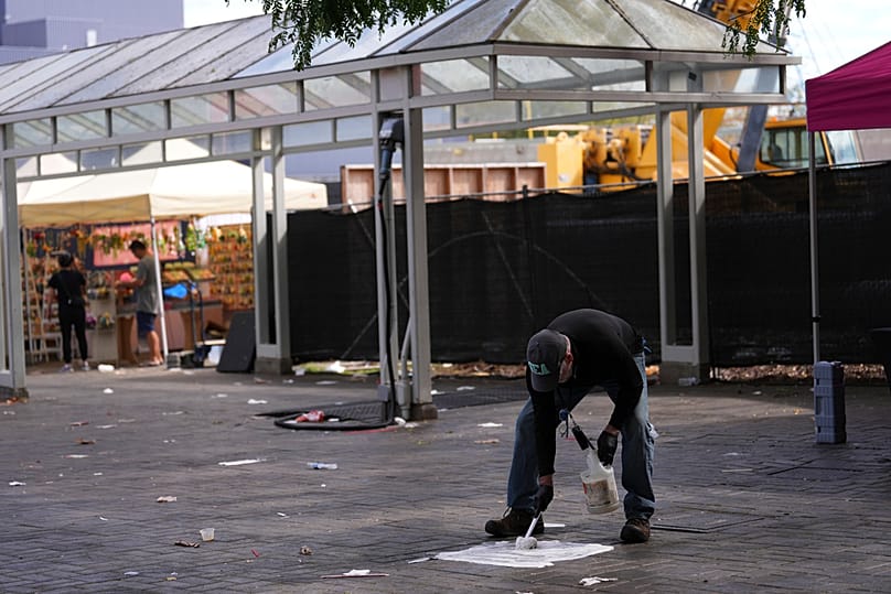 A worker cleans blood off the pavement the day after a shooting at Seattle Center during the Bite of Seattle food festival, Monday, July 27, 2026