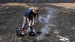 A woman pours water on smoldering grass after wildfires raged in the village of Le Porge, on the Bay of Biscay, France, Monday, July 27, 2026.