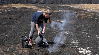A woman pours water on smoldering grass after wildfires raged in the village of Le Porge, on the Bay of Biscay, France, Monday, July 27, 2026.