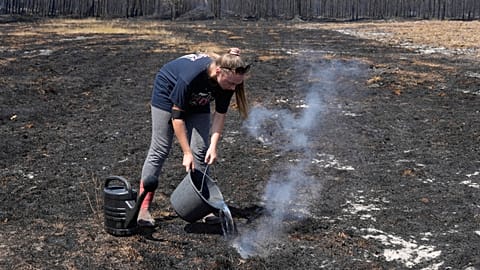 A woman pours water on smoldering grass after wildfires raged in the village of Le Porge, on the Bay of Biscay, France, Monday, July 27, 2026.