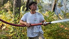 Un hombre sostiene una manguera contra incendios mientras intenta apagar un fuego cerca de Lacanau, con incendios forestales junto a Burdeos, 27 de julio de 2026.