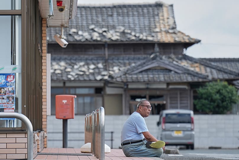 A person sits near a house damaged following an earthquake in Uki, Kumamoto Prefecture, southern Japan, Thursday, July 30, 2026