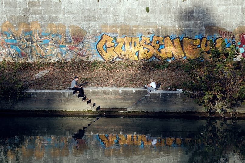 ARŞİV: 15 Kasım 2018 Perşembe, Roma. İnsanlar, düşen yapraklarla kaplı ve otların büyüdüğü Tiber Nehri kıyısında, graffitilerle dolu duvarların fon oluşturduğu bir ortamda oturuyor.