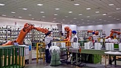 Trabalhadores enrolam rolos de fibra de vidro junto a braços robóticos numa fábrica em Jiujiang, na província de Jiangxi, no centro da China.