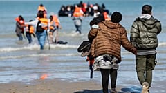 Migrantes correm pela praia para embarcar num pequeno barco rumo ao Reino Unido, em Gravelines, no norte de França.