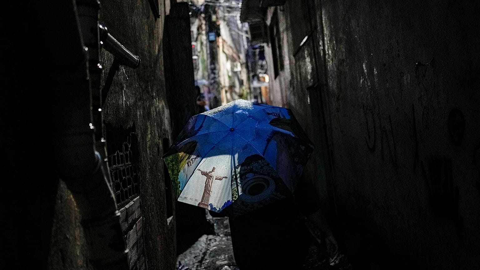 ARQUIVO - Uma mulher caminha por um beco, protegendo-se com um guarda-chuva com a imagem da estátua do Cristo Redentor, na favela da Rocinha,