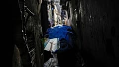 ARQUIVO - Uma mulher caminha por um beco, protegendo-se com um guarda-chuva com a imagem da estátua do Cristo Redentor, na favela da Rocinha,