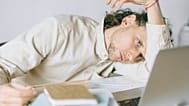 موظف مرهق يجلس إلى مكتبه، تبدو عليه علامات التعب والضغط النفسي، في صورة تجسد الإرهاق المهني في مكان العمل.
