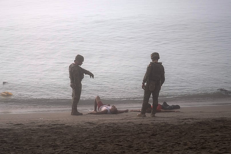 Spanish army soldiers stand next to migrants who swam from Morocco to the Spanish enclave of Ceuta, Saturday, Aug. 1, 2026.