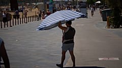 Um homem segura um guarda-chuva enquanto caminha junto a uma praia de Barcelona, Espanha, na quarta-feira, 27 de maio de 2026.