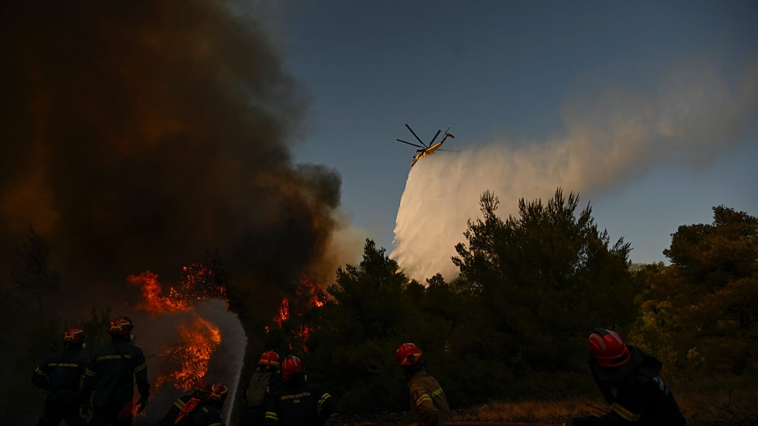 A firefighting helicopter drops water over a smoke-filled forest during a wildfire near Porto Germeno, 2 August, 2026