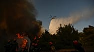 A firefighting helicopter drops water over a smoke-filled forest during a wildfire near Porto Germeno, 2 August, 2026