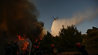 A firefighting helicopter drops water over a smoke-filled forest during a wildfire near Porto Germeno, 2 August, 2026