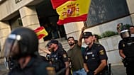 El político de extrema derecha Alvise Pérez ondea una bandera española bajo protección policial mientras los vecinos de Ceuta protestan por su presencia, el sábado 1 de agosto