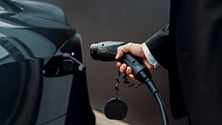 Άνδρας με κοστούμι φορτίζει το ηλεκτρικό του όχημα (EV)