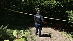 Un poliziotto del Kosovo sorveglia il sito dove le squadre forensi hanno iniziato gli scavi di una fossa comune vicino al villaggio di Kalluder, mercoledì 29 luglio 2026