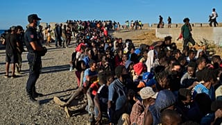 Migrants who crossed from Morocco into Spain line up for food distribution on a beach in the Spanish enclave of Ceuta, 3 August, 2026