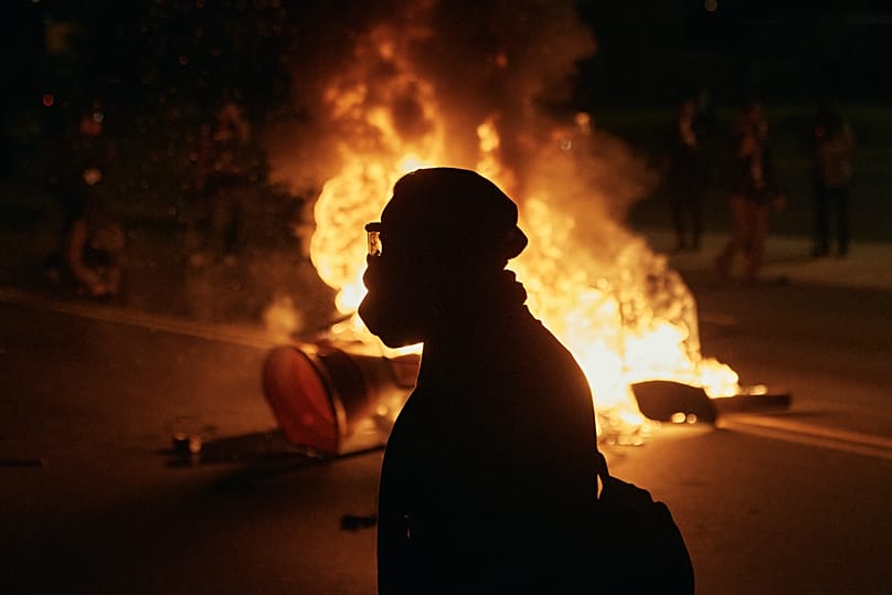 A man wearing protective gear walks in front of a burning barricade outside the Delaney Hall detention centre in Newark, 30 May, 2026