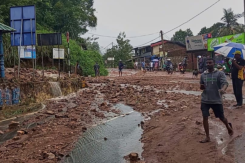 People walk across a mud covered road following heavy rain in Nawalapitiya, 4 August, 2026