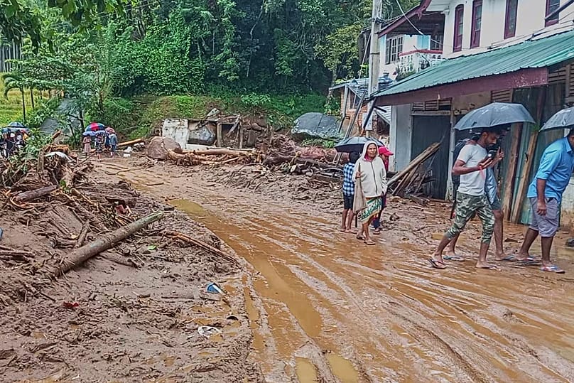 People walk across a mud covered road following heavy rain in Nawalapitiya, 4 August, 2026