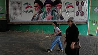 نساء يمررن أمام لافتة تظهر صور المؤسس الثوري الإيراني الراحل آية الله الخميني، على اليسار، والمرشد الأعلى آية الله مجتبى خامنئي، في الوسط، والمرشد الأعلى الراحل آية الله علي خ