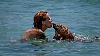 Una mujer besa a su perro mientras nada en una playa de Barcelona, ​​España, el lunes 17 de julio de 2023.