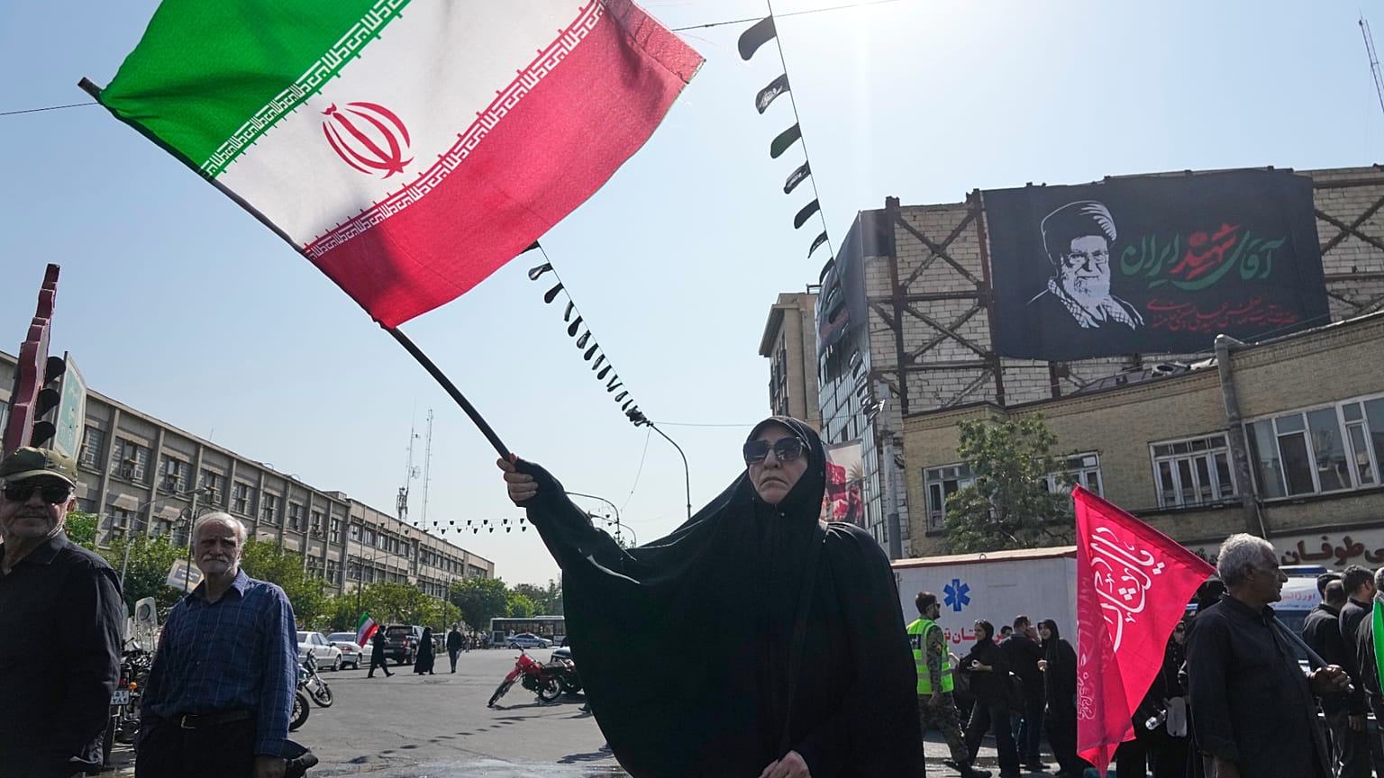 امرأة تلوّح بعلم إيران خلال شعائر الأربعين في طهران، وخلفها لافتة للمرشد الأعلى الراحل علي خامنئي، 4 أغسطس 2026.