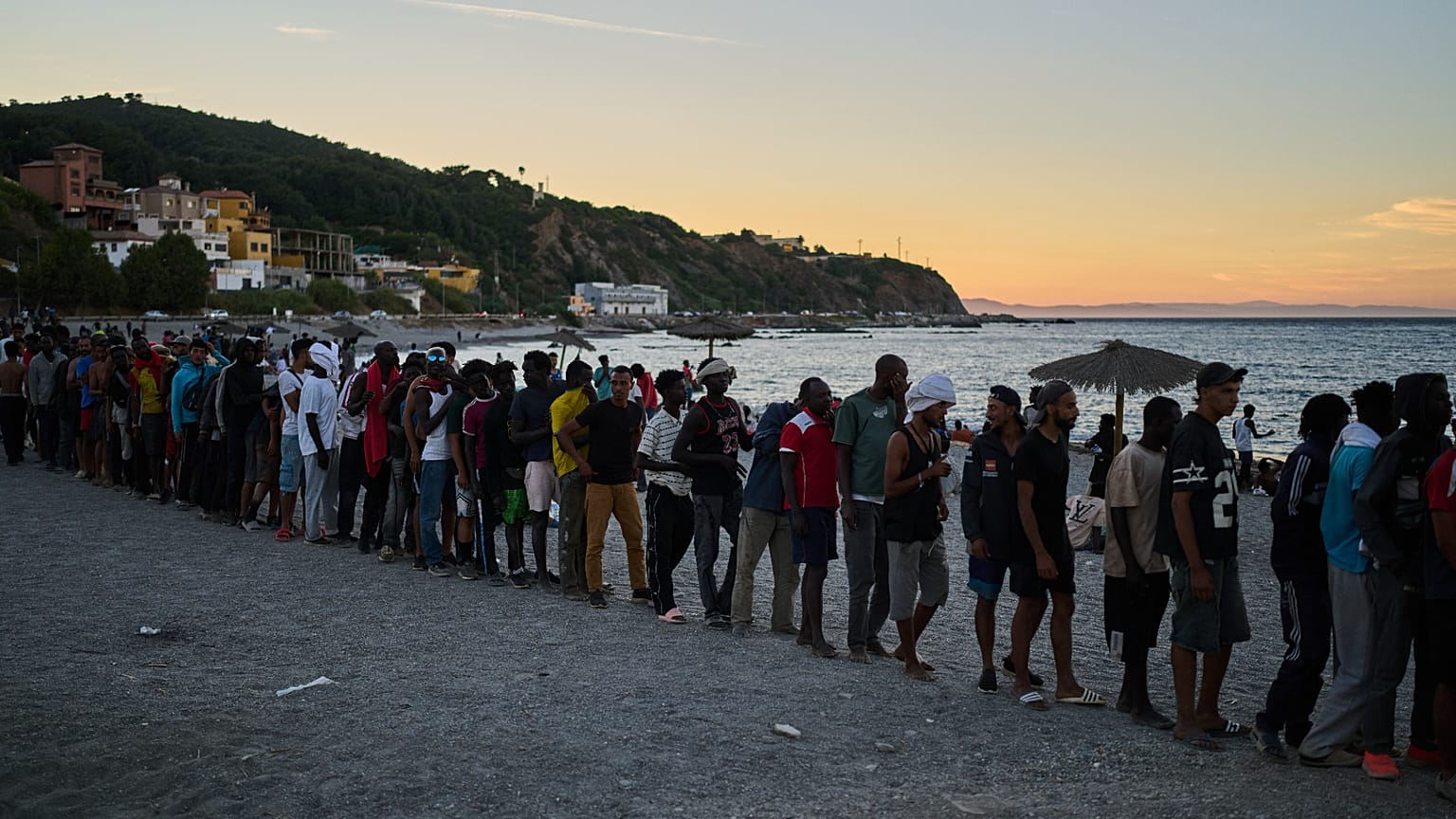 Migrants who crossed from Morocco into Spain line up for food distribution on a beach in the Spanish enclave of Ceuta, Monday, Aug. 3, 2026.