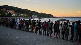Migrants who crossed from Morocco into Spain line up for food distribution on a beach in the Spanish enclave of Ceuta, Monday, Aug. 3, 2026.