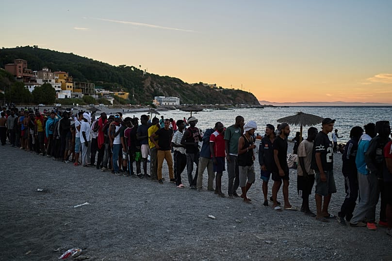 Migrants who crossed from Morocco into Spain line up for food distribution on a beach in the Spanish enclave of Ceuta, 3 August, 2026