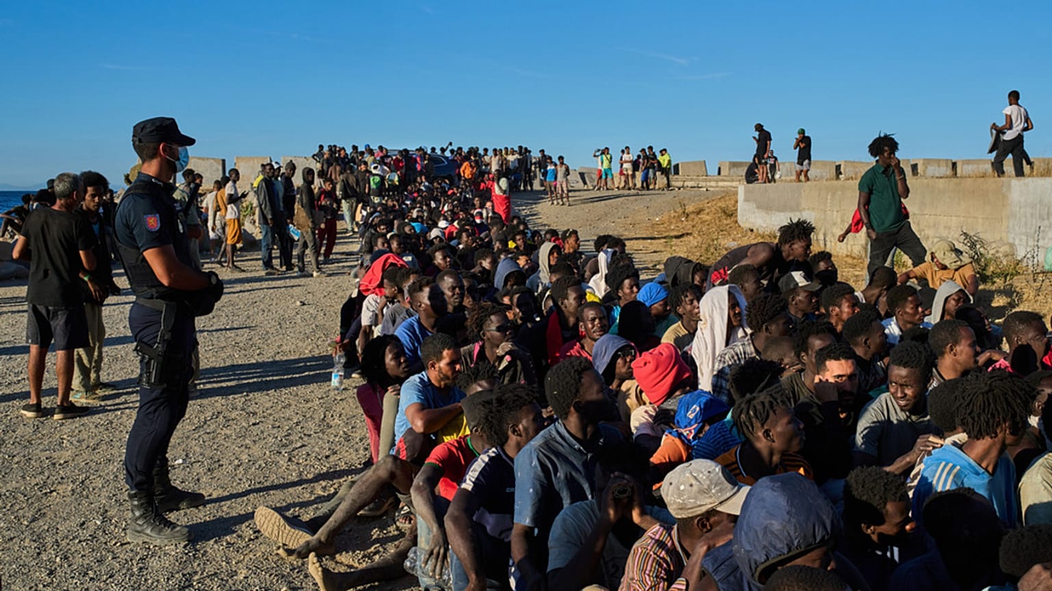 Migrants who crossed from Morocco into Spain line up for food distribution on a beach in the Spanish enclave of Ceuta, 3 August 2026