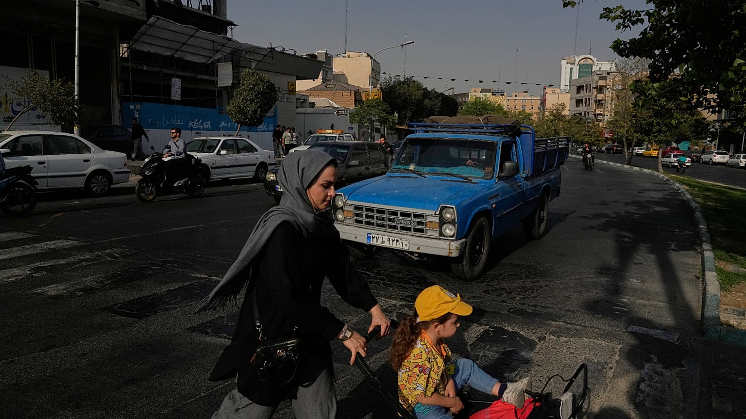 امرأة تعبر الشارع مع فتاة في وسط مدينة طهران، إيران، الأربعاء 22 يوليو 2026. (AP Photo/فاهد سليمي)