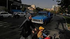 امرأة تعبر الشارع مع فتاة في وسط مدينة طهران، إيران، الأربعاء 22 يوليو 2026. (AP Photo/فاهد سليمي)