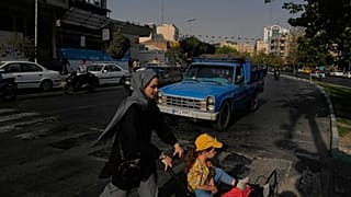 امرأة تعبر الشارع مع فتاة في وسط مدينة طهران، إيران، الأربعاء 22 يوليو 2026. (AP Photo/فاهد سليمي)