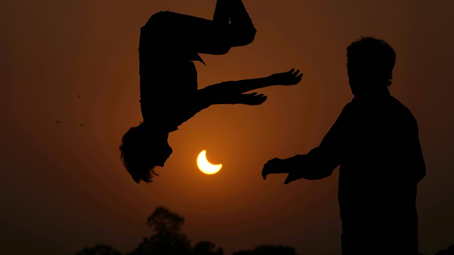 Dos jóvenes saltan en un trampolín en las afueras de Lahore, Pakistán, en un eclipse parcial del 25 de octubre de 2022