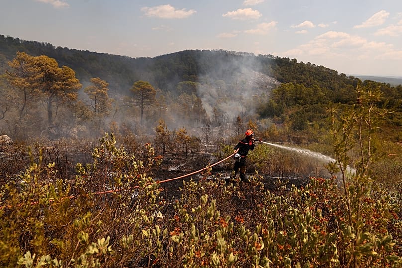 Un pompier arrose la végétation calcinée lors d'une opération de nettoyage dans une zone touchée par un feu de forêt à Cotignac, en France, le mercredi 22 juillet 2026