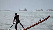 A man paddles a stand-up paddleboard as cargo ships and other commercial vessels appear anchored in the Strait of Hormuz off Bandar Abbas, Iran, Monday, July 27, 2026