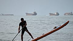 A man paddles a stand-up paddleboard as cargo ships and other commercial vessels appear anchored in the Strait of Hormuz off Bandar Abbas, Iran, Monday, July 27, 2026
