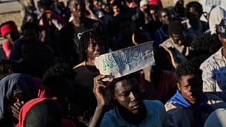 Un migrante que cruzó de Marruecos a España sostiene un cartel que dice "asilo" mientras hace cola para conseguir comida en una playa de Ceuta, el lunes 3 de agosto de 2026.