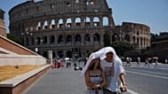 FILE - Tourists take shelter as they walk in front of the Rome'a ancient Colosseum, Aug. 1, 2026. 
