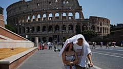 FILE - Turistas abrigam-se enquanto caminham em frente ao antigo Coliseu de Roma, 1 de agosto de 2026