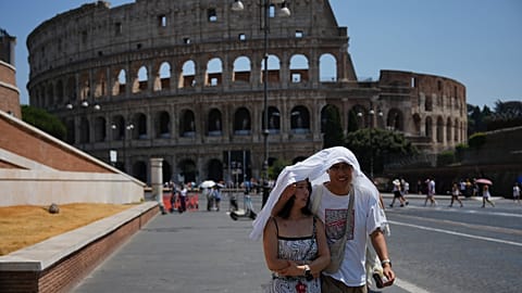 FILE - Tourists take shelter as they walk in front of the Rome'a ancient Colosseum, Aug. 1, 2026. 