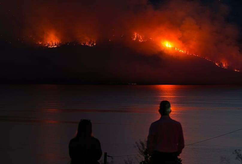 ARCHIVIO - Alcune persone a Lake Country, in British Columbia, osservano l’incendio Quilpituk Creek bruciare sul versante della montagna oltre il lago Okanagan, vicino Fintry, 3 agosto 2026. 