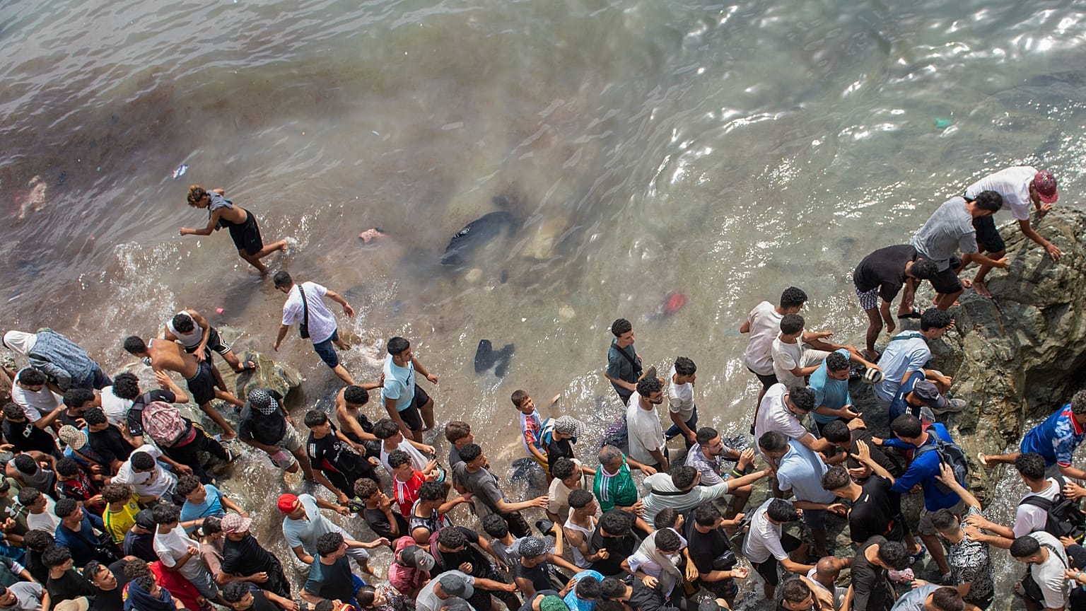 Alcune persone camminano lungo una spiaggia mentre cercano di attraversare dalla città marocchina di Fnideq all'enclave spagnola di Ceuta, venerdì 31 luglio 2026.