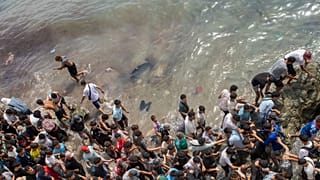 Varias personas caminan por una playa mientras intentan cruzar desde la ciudad marroquí de Fnideq hasta el enclave español de Ceuta, el viernes 31 de julio de 2026.