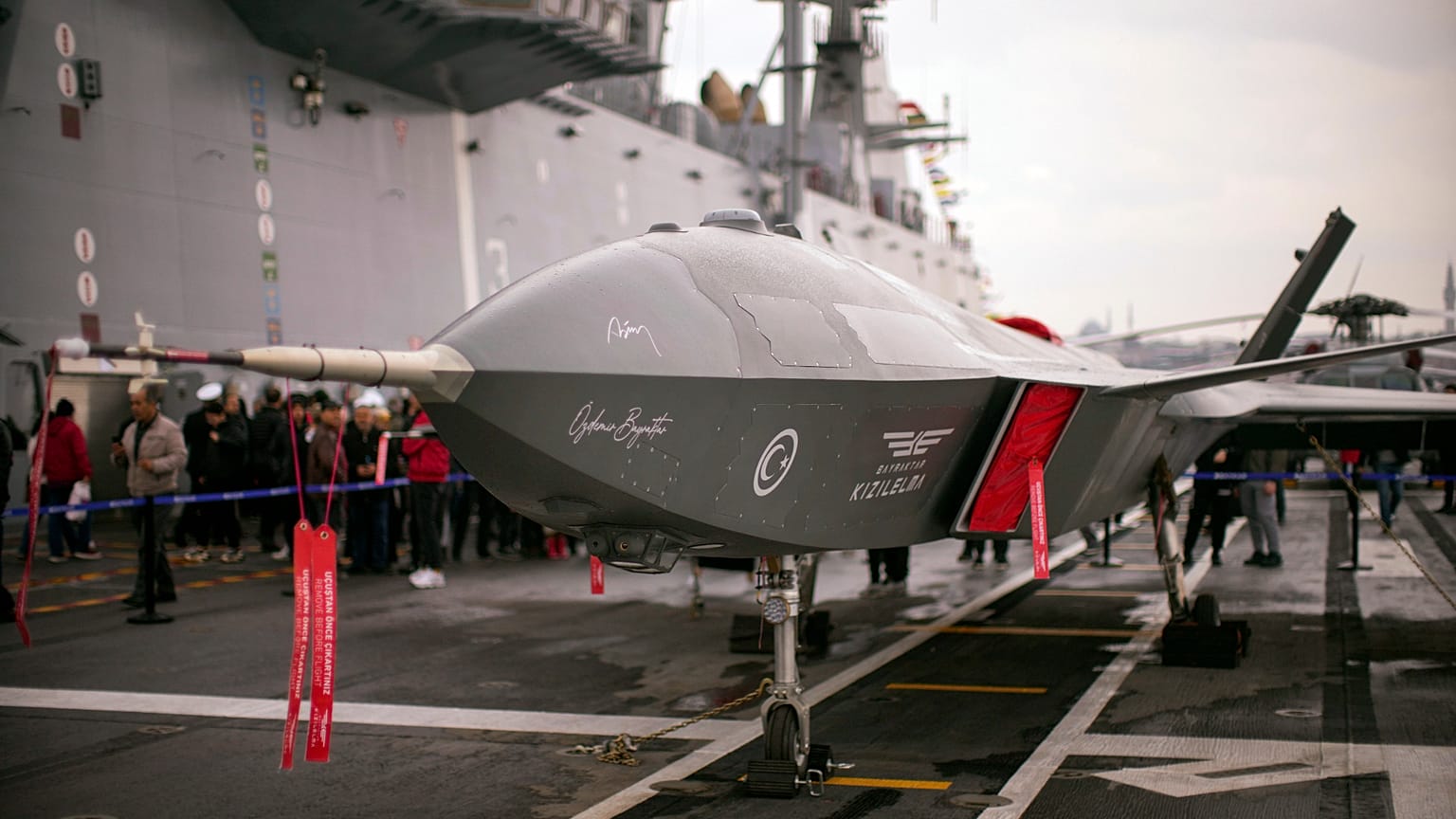 People stand next to an unmanned combat aerial vehicle (UCAV) Bayraktar Kizilelma on board the Turkish amphibious assault ship TCG Anadolu L400, anchored in Istanbul, Turkey, 