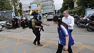 A schoolgirl walks past a policeman keeping guard after a shooting at the Debsirin Nonthaburi School in Thailand's Nonthaburi province, 7 August, 2026