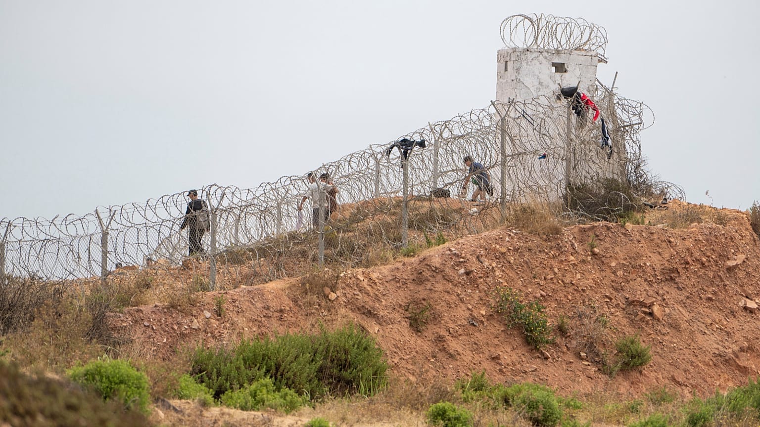 Varias personas pasan junto a una alambrada en la localidad marroquí de Fnideq, al norte del país, mientras intentan cruzar a Ceuta, el viernes 31 de julio de 2026. (Foto AP)